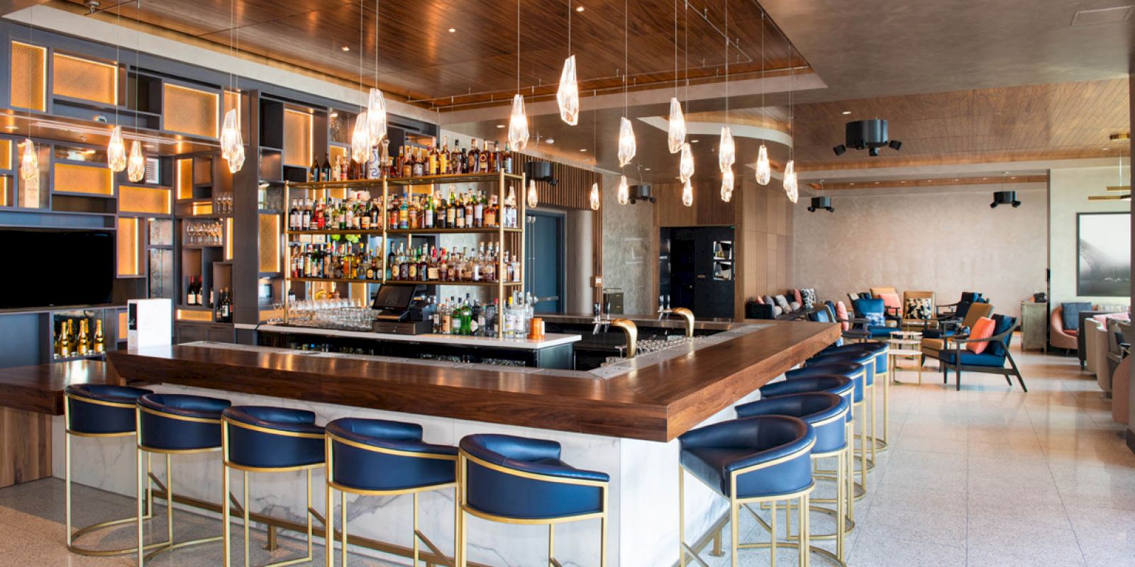 A modern bar with stylish seating, a well-stocked selection of bottles, and elegant lighting. The space has a warm, inviting ambiance.