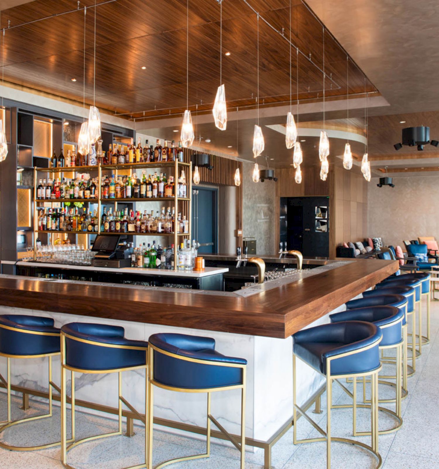 A stylish bar with counter seating, pendant lighting, and a fully stocked back bar. There are lounge chairs in the open space beyond.