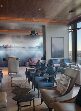 A modern lounge with plush seating, large windows offering a waterfront view, artwork on the wall, and a serene atmosphere.