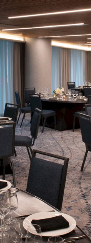 The image shows an elegantly set dining room with round tables, chairs, wine glasses, and tableware, ready for an event or banquet.
