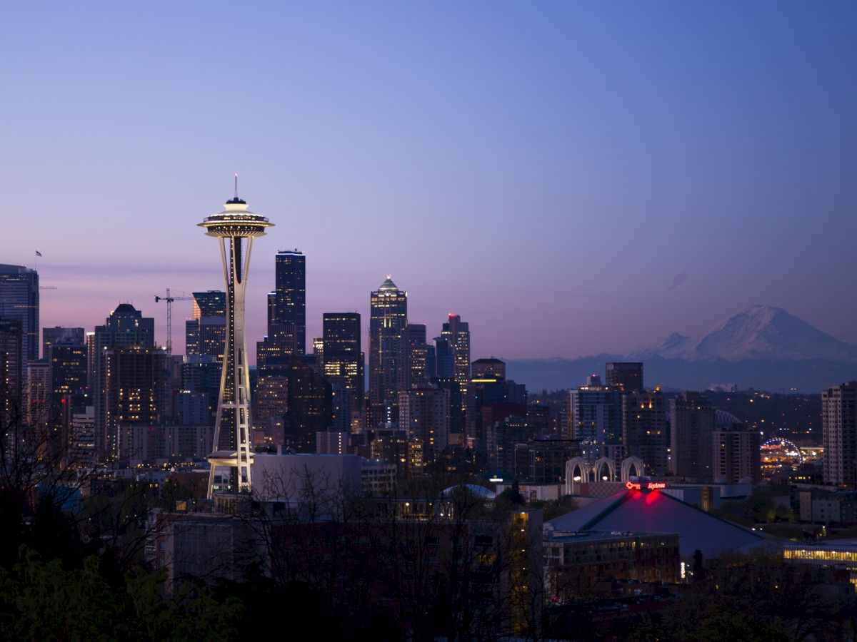 Seattle skyline at dusk, featuring the Space Needle, downtown buildings, and Mount Rainier in the background.