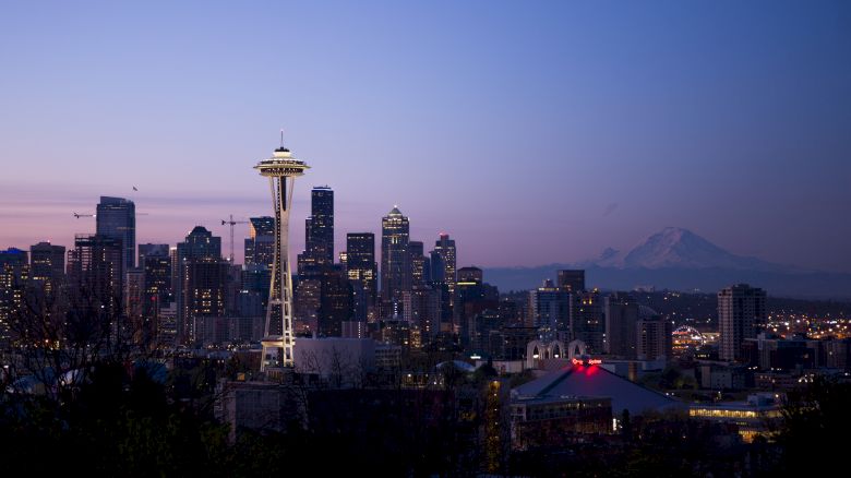 Seattle skyline at dusk, featuring the Space Needle, downtown buildings, and Mount Rainier in the background.