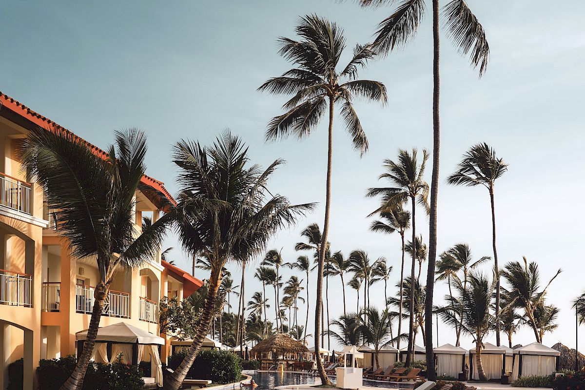 A tropical resort scene with a pool, lounge chairs, and tall palm trees under a clear sky, creating a relaxing atmosphere.